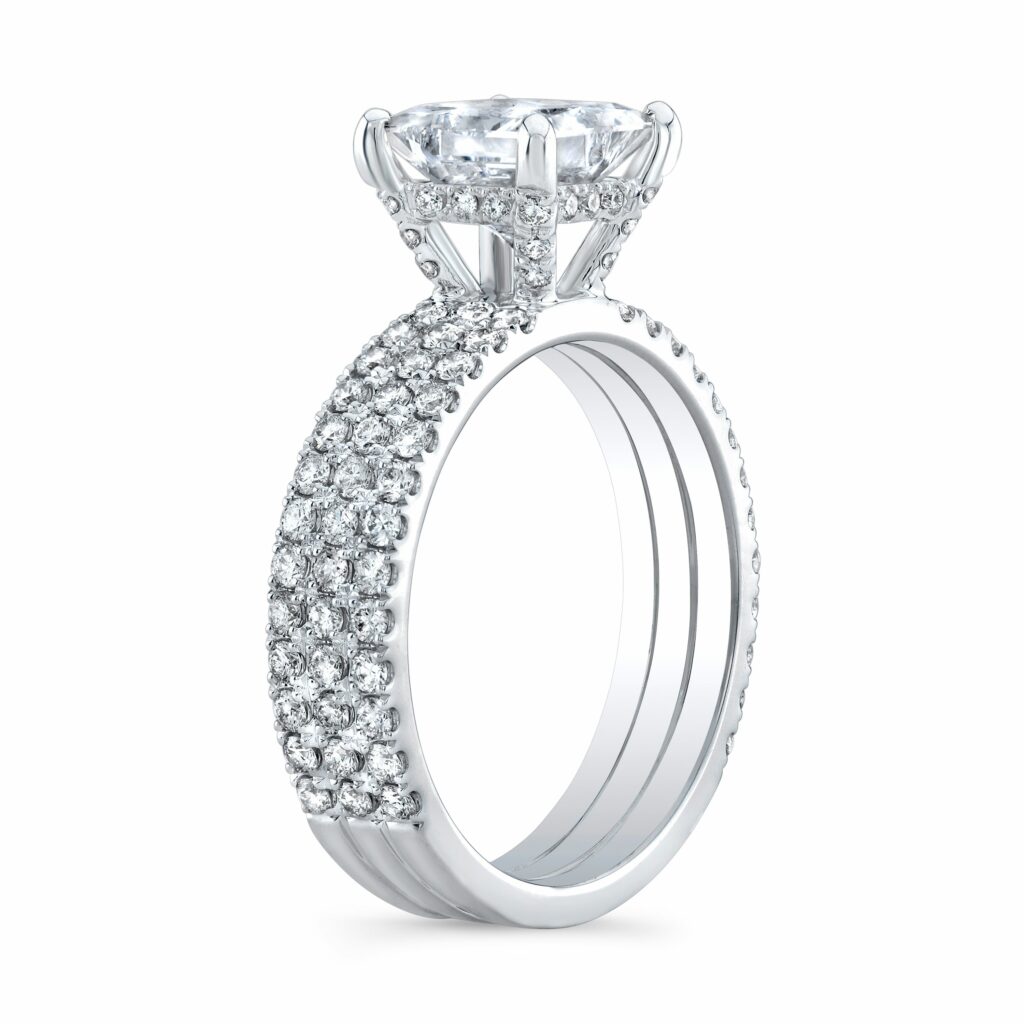Featuring 3 rows of pave diamonds that go 3 quarters of the way and is finished by a hidden halo setting with a princess cut center